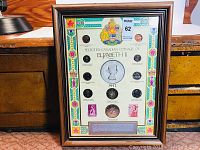 Full view of framed coin and stamp collection showing decorative board, coins and stamps