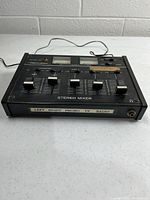 Front angled view of Realistic stereo mixer showing sliders, VU meters, and integrated power cord