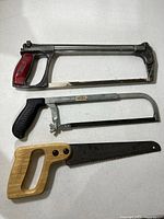 Three hacksaws grouped: large red-handled, medium black-handled, small wood-handled