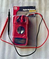 Front view of packaged red digital multimeter with attached test leads