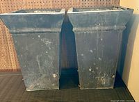 Front view of both metal urn planters showing overall shape and exterior wear