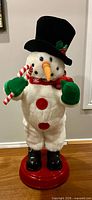 Full view of plush battery operated snowman on red base with accessories
