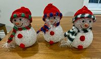 Three acrylic light-up snowmen figurines on wooden surface