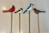 Four painted wooden bird figures on sticks displayed on light countertop