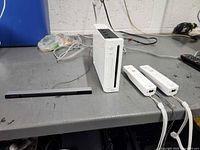 Wii console, sensor bar, two Wii Remotes and cables on workbench