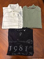 All three shirts laid out: white polo, green crew neck, black graphic shirt