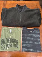 All three garments laid out: black fleece jacket folded above two T-shirts