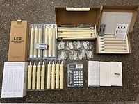 All contents of lot laid out: 32 candles in trays, remotes, string lights, adhesive dots, grippers, boxes