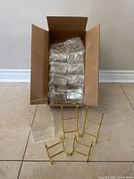 Box containing individually wrapped clear plastic brochure holders and four gold metal stands placed in front