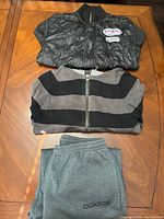 All three clothing items laid out: black quilted Jets jacket, grey/black striped jacket, grey Adidas sweatpants