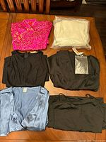 All six dresses folded on table: fuchsia, cream (bagged), three black, light blue