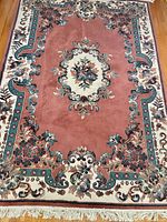 Full view of rug showing pink field, cream medallion, floral border and fringe