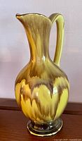 Front view of ceramic pitcher showing drip-glaze pattern and gilded rim and foot