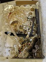 Box with assorted faux pearl necklaces, lucite beads, brooches, bracelets, earrings, and straight razor