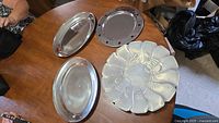 All four trays on table: two plain oval, one round star-rim, one embossed scalloped round