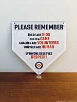 Front view of the home-plate shaped metal sign showing full printed text and size reference coin