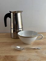 Moka pot, china cup and spoon grouped on tabletop