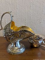 Side view of floral embossed sugar scuttle with gold interior alongside creamer