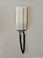 Front view of phone base mounted on wall with coiled cord hanging