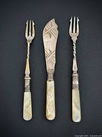 Front view of two pickle forks and etched butter spreader showing decorative details and handles
