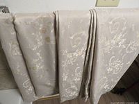 Group of beige floral curtain panels draped over surface