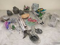 Overview of assorted wind chime sets, tubes, painted tops, stained glass bird panels and resin bird ornaments on table