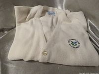Folded off-white sweater showing button front and embroidered logo