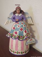 Front view of Jim Shore quilting angel figurine with hang tag visible