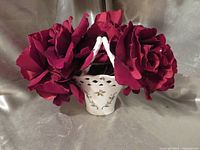 Front view of porcelain basket with handle and holly motif, filled with burgundy roses