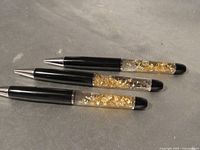 Three black pens with clear sections holding gold flakes