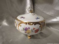Front view of porcelain footed lidded dish showing floral design and gold scrollwork