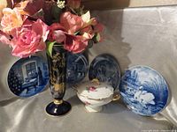 Group shot of vase with artificial flowers, covered dish, four blue plates