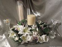 Floral centerpiece on Mikasa cake stand with short pillar candle, tall wrapped candle behind, crystal candlesticks on either side
