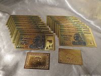Array of twenty gold-foil banknotes and two certificate cards on fabric background