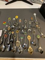 Overhead view of 22 souvenir spoons and 3 pins laid out on black background