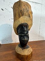 Front view of carved wooden bust with tall raw wood headdress