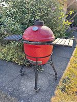 Full view of red Kamado Joe ceramic grill on cart with folding wooden side shelves