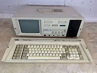 Front view of portable computer showing built-in CRT, controls, floppy drive and detached keyboard