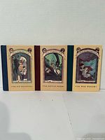 Front view of three hardcover books standing upright showing cover art and titles