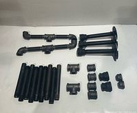 Assortment of black steel threaded pipes, elbows, tees, flanges, couplings and caps laid out on white background