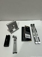 All four tech accessories laid out: foldable laptop stand, tablet stand, Otofly iPhone case with packaging, compact mini tripod