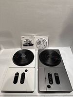 Two DJ Hero turntable controllers and DJ Hero 2 game disc with case displayed against white backdrop