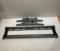 All components of metal TV wall mount laid out: long horizontal rail and two adjustable arm plates