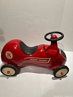 Side view of red Radio Flyer ride-on toy car showing seat, steering wheel, decals and wheels