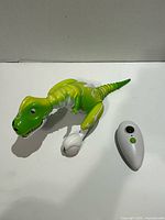 Overall view of green and white T-Rex toy with its white remote control on white background