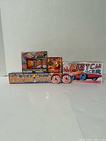 Front view of all six unopened tin toys and games: Jetcar Racer box, tin racecar box, Snake Charmer top box, Marble Game box, two Pinocchio tops