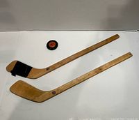 Top-down view of two wooden mini hockey sticks and one puck
