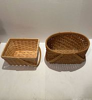 Two woven wooden baskets side by side: rectangular with handle and oval with crossover straps