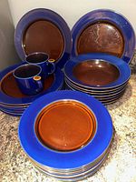 Stacked dinner plates, bowls, and mugs showing blue rim and brown center