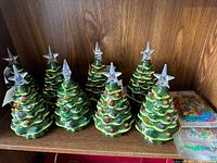 Front view of eight ceramic Christmas trees with star toppers and three packs of plastic pegs